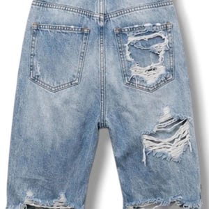 Op de afbeelding: Lichtblauwe spijkershort met een hoge taille, riemlussen en een beige leren label op de achterband met de tekst SPBY. De short heeft twee achterzakken, zware slijtageplekken, gerafelde randen en grote scheuren in de rechter broekspijp.