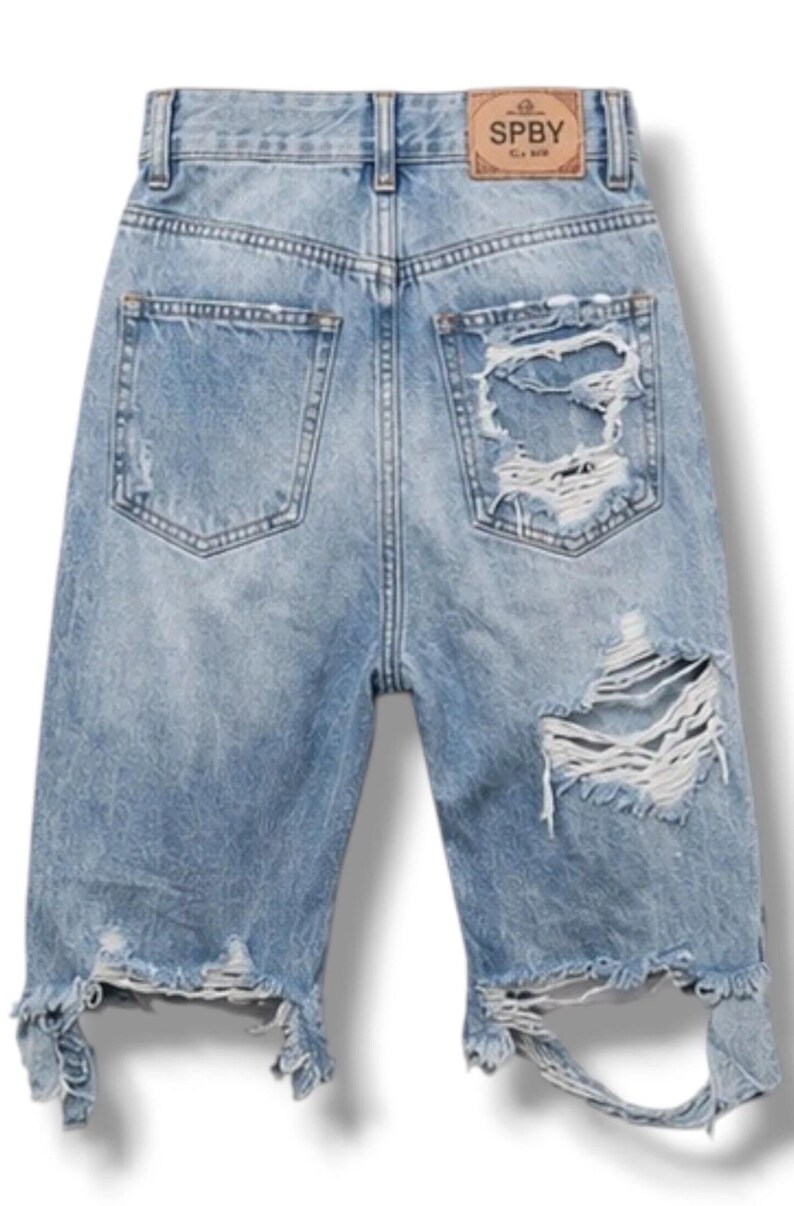 Op de afbeelding: Lichtblauwe spijkershort met een hoge taille, riemlussen en een beige leren label op de achterband met de tekst SPBY. De short heeft twee achterzakken, zware slijtageplekken, gerafelde randen en grote scheuren in de rechter broekspijp.