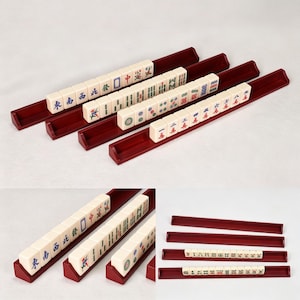 Könnte beinhalten: Vier dunkelrote Mahjong-Fliesenhalter aus Holz, die in einer Reihe angeordnet sind und jeweils eine Reihe cremefarbener Spielsteine mit verschiedenen blauen, grünen und roten chinesischen Schriftzeichen und Symbolen enthalten.