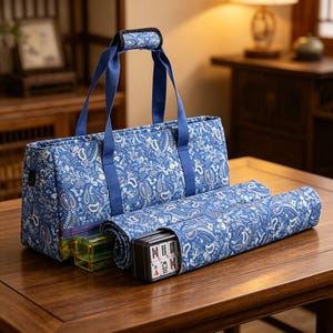 May include: A blue fabric carrying bag with a white paisley pattern, featuring two blue handles and a padded grip. Beside the bag lies a matching blue paisley fabric mat rolled up, containing a black case filled with white mahjong tiles.
