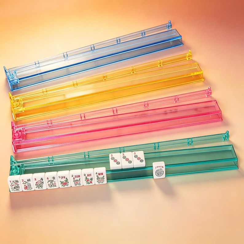 May include: Four long, rectangular, translucent plastic mahjong tile racks in blue, yellow, pink, and teal. The teal rack holds several white mahjong tiles with red, green, and black symbols, including numbers and floral designs, plus one Joker tile.