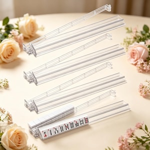 May include: A set of four clear acrylic mahjong tile racks. Each rack features a long, narrow channel for holding tiles. One rack is shown with a row of white mahjong tiles featuring black and red characters and symbols arranged horizontally.