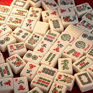 May include: A collection of off-white Mahjong tiles scattered across a surface, featuring various red, green, and black engraved symbols, numbers, and characters, including specific tiles labeled with text such as WIN, SUM, SPR, AUT, and JOKER.