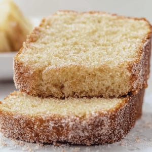 Peut inclure: Deux tranches de gâteau doré, recouvertes d'un enrobage de sucre et de cannelle. Le gâteau a une texture légère et aérée et un extérieur légèrement croustillant. L'image est un gros plan, mettant en évidence les détails du gâteau.
