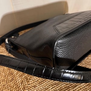 May include: A black shoulder bag featuring a textured pebbled leather body and a smooth, glossy strap with a crocodile-embossed pattern. The bag includes silver-toned metal hardware connecting the strap to the main compartment.