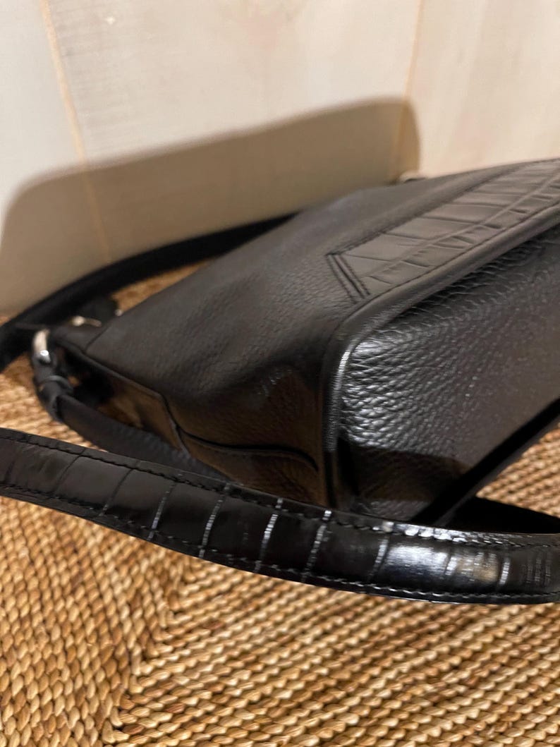 May include: A black shoulder bag featuring a textured pebbled leather body and a smooth, glossy strap with a crocodile-embossed pattern. The bag includes silver-toned metal hardware connecting the strap to the main compartment.