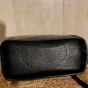 May include: A black rectangular bag with a textured surface featuring a prominent embossed heart shape on the front panel. The bag has a structured frame with smooth edges and a distinct crocodile-like pattern along the top border.