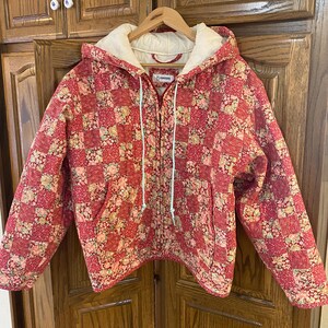 May include: A white ceramic mug with a black handle and the text "But First, Coffee" in a bold, black font. The mug is set against a blurred background, suggesting a cozy setting.