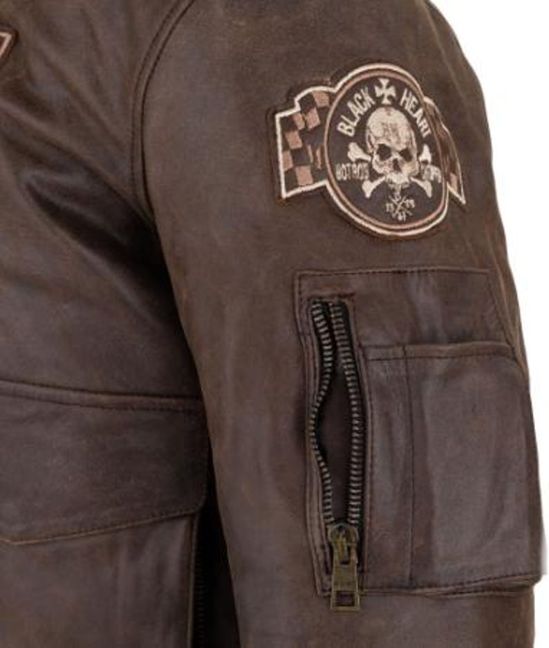 Op de afbeelding: Bruine leren jas met een schedel- en gekruiste botten-patch met de tekst "Black Heart Hot Rods". De jas heeft een zak met ritssluiting op de mouw en twee voorzakken. Het leer heeft een distressed look.