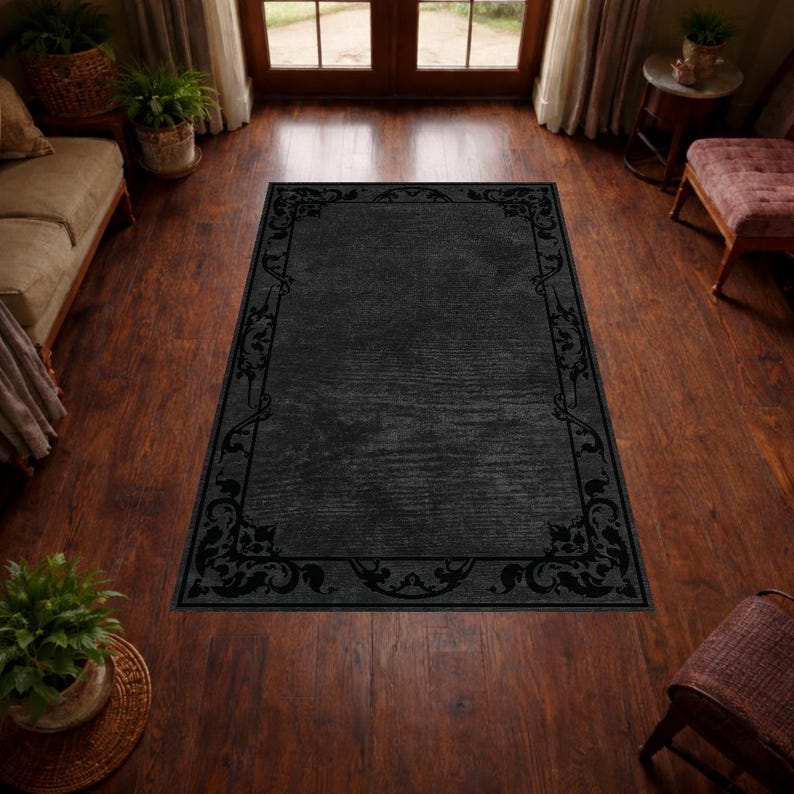 Puede incluir: Una alfombra rectangular negra con un borde decorativo con dise&ntilde;os florales y de volutas. La alfombra est&aacute; colocada sobre un suelo de madera y la habitaci&oacute;n est&aacute; iluminada con luz natural.