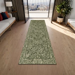 May include: A green and cream-colored runner rug with a floral pattern. The rug is rectangular and features a repeating design of stylized leaves and branches. The rug is placed on a hardwood floor.