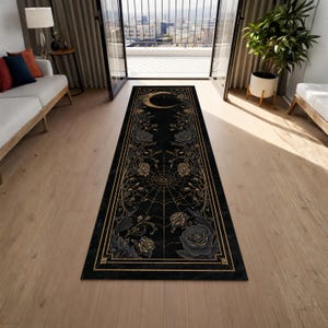May include: Black rectangular rug with a gold border and floral and spiderweb design. The rug features a crescent moon at the top and roses and vines throughout. The rug is placed on a wooden floor.