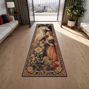 Könnte beinhalten: Ein rechteckiger Teppich mit einem klassischen Design, das eine Frau, ein Einhorn und Blumen zeigt. Der Teppich hat einen schwarzen Rand mit goldenen Akzenten. Die Frau trägt ein blaues und pfirsichfarbenes Kleid. Das Einhorn ist weiß. Der Teppich liegt auf einem Holzboden.