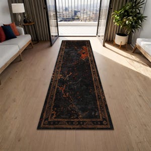 May include: A rectangular, dark gray rug with an intricate border and a central design featuring orange and brown accents. The rug is placed on a light-colored wooden floor, adding a touch of elegance to the room.