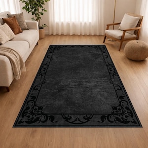 Puede incluir: Una alfombra rectangular negra con un borde decorativo con dise&ntilde;os florales y de volutas. La alfombra tiene un aspecto texturizado y est&aacute; colocada sobre un suelo de madera. La alfombra es de color gris oscuro.
