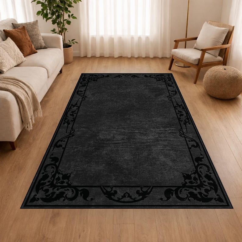 Puede incluir: Una alfombra rectangular negra con un borde decorativo con dise&ntilde;os florales y de volutas. La alfombra tiene un aspecto texturizado y est&aacute; colocada sobre un suelo de madera. La alfombra es de color gris oscuro.
