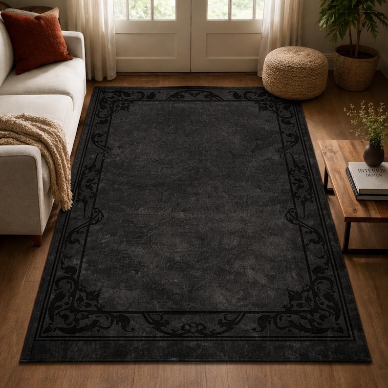 Puede incluir: Una alfombra rectangular grande de color carb&oacute;n con un borde oscuro y ornamentado. La alfombra tiene una apariencia desgastada y texturizada, agregando profundidad. El borde presenta un dise&ntilde;o floral y de volutas repetido.