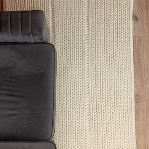 Puede incluir: Vista a&eacute;rea de una secci&oacute;n de un sof&aacute; de terciopelo gris oscuro junto a una alfombra de punto grueso de color crema. La alfombra est&aacute; hecha de hilo grueso y tiene un aspecto texturizado. El suelo es de madera marr&oacute;n claro.