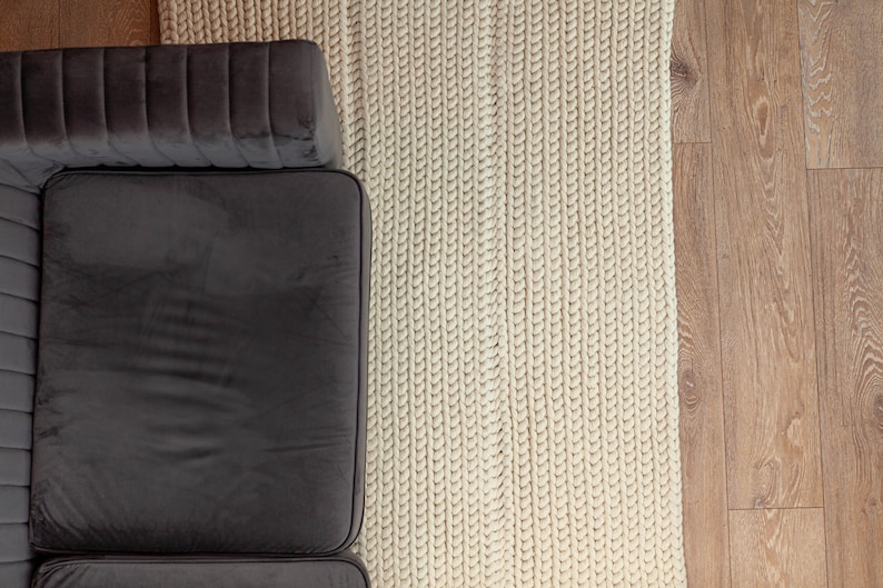 Puede incluir: Vista a&eacute;rea de una secci&oacute;n de un sof&aacute; de terciopelo gris oscuro junto a una alfombra de punto grueso de color crema. La alfombra est&aacute; hecha de hilo grueso y tiene un aspecto texturizado. El suelo es de madera marr&oacute;n claro.