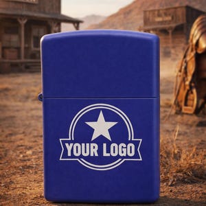 Può includere: Un accendino blu cobalto con una stella bianca e la scritta "YOUR LOGO" in uno stendardo bianco. L'accendino è ambientato su uno sfondo desertico con un saloon e montagne sullo sfondo.