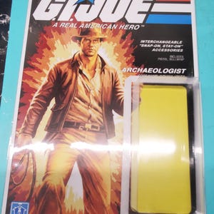 May include: G.I. Joe action figure of an archaeologist, packaged on a blue and white card. The card features an illustration of the character with a pistol and bullwhip. The packaging includes the text "A Real American Hero".