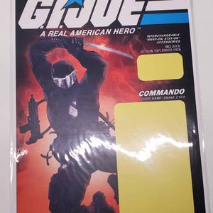 May include: A G.I. Joe A Real American Hero action figure card featuring Snake Eyes in a black uniform with a sword. The packaging includes text such as Fully Poseable Modern Army Figure, Ages 5 & Up, Commando, and Code Name: Snake Eyes.