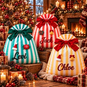 Può includere: Tre sacchi regalo natalizi in tessuto con strisce verticali color ottanio, rosso e giallo. Ogni sacco presenta un grande fiocco in tessuto sulla parte superiore, un piccolo ornamento decorativo e un nome ricamato in corsivo: Levi, Jack e Chloe.