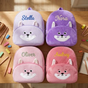 Puede incluir: Cuatro mochilas personalizadas con temática de zorro en tonos morados y rosas. Cada mochila presenta un diseño de cara de zorro con detalles bordados y los nombres "Stella", "Nora", "Oliver" y "Audrey". Las mochilas tienen un patrón de rayas y un asa superior.