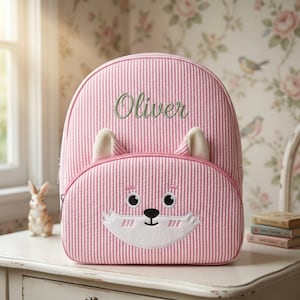 May include: Pink and white striped backpack with a fox face design on the front. The backpack has a top handle, adjustable straps, and the name "Oliver" embroidered in green. The fox face has white accents and black eyes.