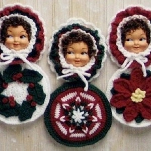 May include: Three crocheted ornaments featuring doll faces with brown hair, each framed by a ruffled border. The ornaments display a holly wreath, a geometric star pattern, and a red poinsettia flower in shades of red, green, and white.