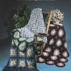 May include: Image of a book cover titled "Amazing Star Afghans" with four crocheted afghans draped over a wooden rocking chair. The afghans feature star and floral patterns in various colors, including blue, green, and black. One afghan has a fringe.