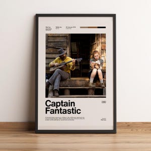 Könnte beinhalten: Ein gerahmtes Filmplakat für Captain Fantastic mit einem zentralen Foto einer Person mit Hut, die eine Akustikgitarre spielt, und einer weiteren Person, die auf einer Holzveranda ein Buch liest. Das Design enthält Text und Farbfelder.