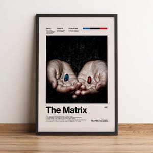 May include: A framed poster for the movie "The Matrix" featuring a pair of hands holding a blue and a red pill. The poster has the movie title in large font, with text at the top and bottom. The background is dark.