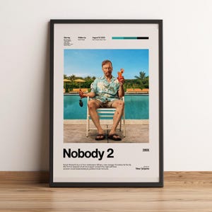 Puede incluir: Un póster de película enmarcado de Nobody 2 que muestra a un hombre con camisa de flores y pantalones cortos sentado en una silla blanca junto a una piscina. El póster incluye el título Nobody 2, la fecha 15 de agosto de 2025 y un resumen.