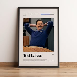 Könnte beinhalten: Ein gerahmtes Poster mit einem zentralen Foto eines lächelnden Mannes mit Schnurrbart in einem marineblauen Pullover, die Hände hinter dem Kopf. Der Text lautet Ted Lasso, 2020, und enthält Details zur Besetzung und eine kurze Zusammenfassung.