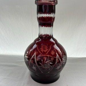 Puede incluir: Una taza de cerámica blanca con un asa negra y el texto "But First, Coffee" en negrita negra. La taza se encuentra sobre un fondo borroso, sugiriendo un ambiente acogedor.