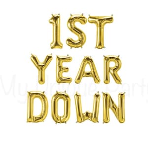 May include: Gold foil balloons spelling out "1ST YEAR DOWN" against a white background. The balloons are arranged to be read from left to right and top to bottom. Perfect for a first-year anniversary celebration.