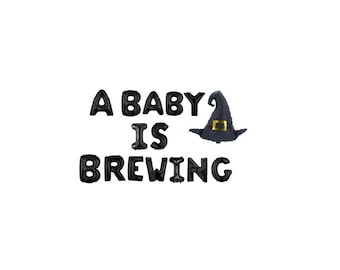 May include: A set of black letter-shaped balloons spelling out the phrase A BABY IS BREWING, accompanied by a black witch hat balloon featuring a gold buckle detail. The balloons are arranged in three lines against a plain white background.