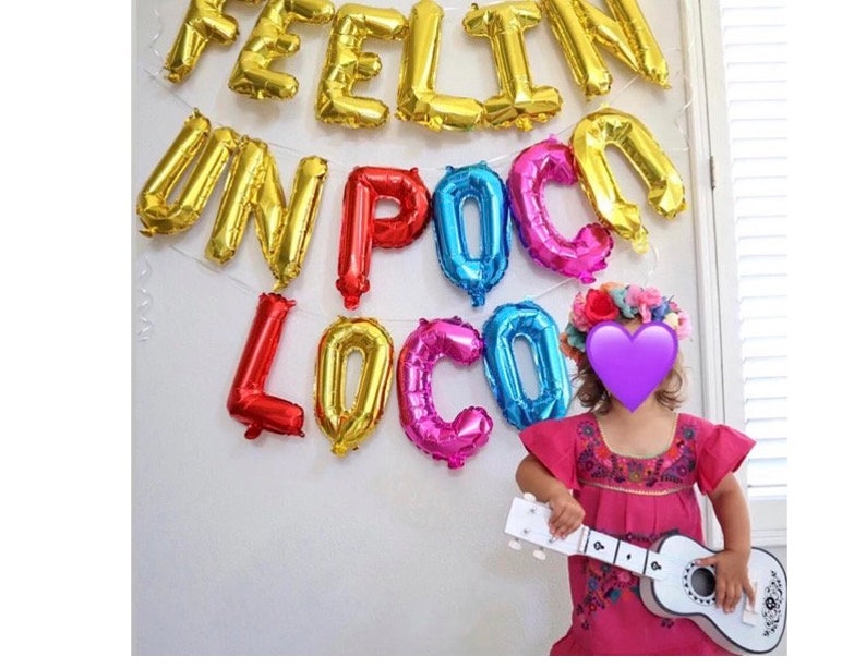 Pu&ograve; includere: Palloncini dorati formano la scritta "FEELIN' UN POCO LOCO" su un muro bianco. Sotto, una bambina con un vestito rosa e una corona di fiori tiene in mano una chitarra giocattolo bianca. I palloncini sono dorati, rossi, blu e rosa.