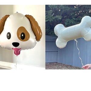 May include: Two foil balloons: one shaped like a dog's head with brown ears and a pink tongue, and another in the shape of a bone. The dog balloon has a white face with brown spots and black eyes. The bone balloon is light green.