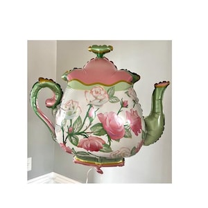 May include: A large, decorative teapot-shaped balloon. The balloon features a floral design with pink roses and green leaves on a white background. The handle and spout are green, and the top is pink and green.