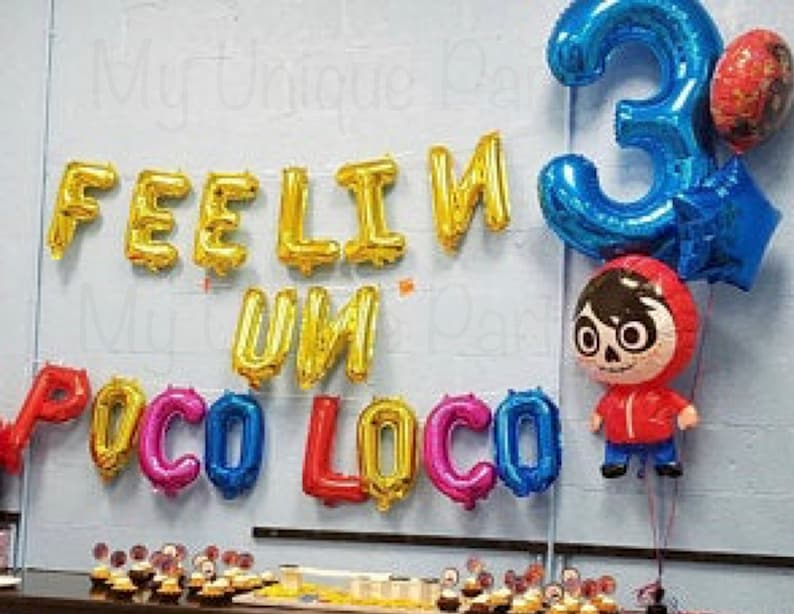 Pu&ograve; includere: Decorazione per festa di compleanno con palloncini in lamina che compongono la scritta "FEELIN' UN POCO LOCO". Un grande palloncino blu con il numero "3", un palloncino a forma di personaggio Coco e altri palloncini colorati. Cupcake sul tavolo.