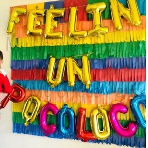 Pu&ograve; includere: Decorazione per feste con palloncini dorati che formano la scritta "FEELIN UN OCOLOC". Lo sfondo &egrave; composto da carta frangiata multicolore, creando un'atmosfera allegra e festosa per celebrare.