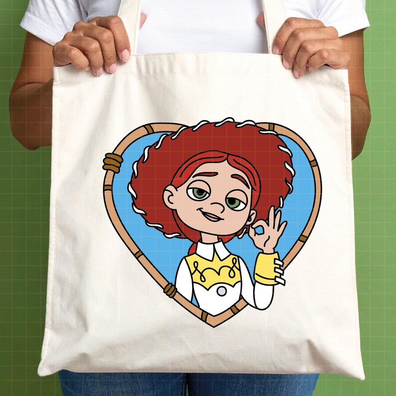 K&ouml;nnte beinhalten: Eine cremefarbene Tragetasche mit einer Cartoon-Illustration einer Figur mit roten Haaren, gr&uuml;nen Augen und einem wei&szlig;en und gelben Outfit. Die Figur befindet sich in einem herzf&ouml;rmigen Rahmen mit blauem Hintergrund.