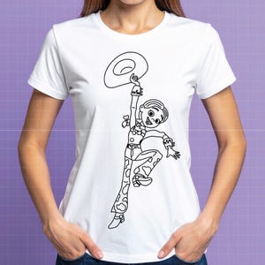 May include: White t-shirt featuring a black and white line drawing of a cartoon cowgirl holding a hat. The cowgirl is wearing a cow-print outfit and a hat. The design is centered on the front of the shirt.