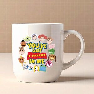 May include: A white ceramic mug featuring a colorful graphic of various cartoon characters arranged in a circle around the text "YOU'VE GOT A FRIEND IN ME" printed in blue and yellow letters on a red background. The mug has a curved handle.