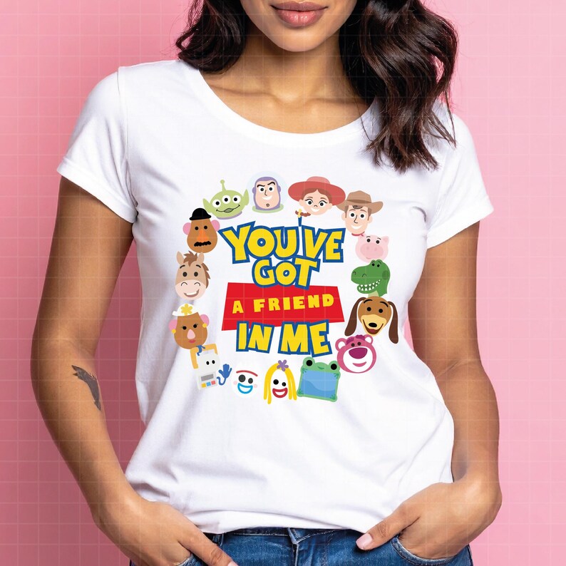May include: A white short-sleeved t-shirt featuring a circular arrangement of various cartoon characters surrounding the text "YOU'VE GOT A FRIEND IN ME" printed in blue and yellow letters over a red rectangular block on the center of the chest.