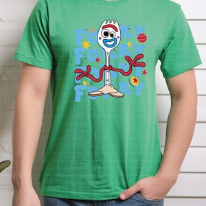 May include: Green t-shirt featuring a cartoon character Forky from Toy Story. The design includes Forky's face, red arms, and the text "Forky" in blue letters. The shirt has a crew neck and short sleeves.