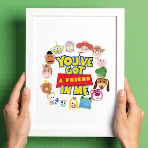 May include: A white framed print featuring the text "YOU'VE GOT A FRIEND IN ME" in blue and yellow letters on a red background. The text is surrounded by a circular arrangement of colorful cartoon character faces including a cowboy, space ranger, and various toys.