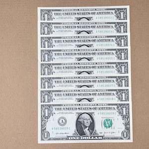 May include: A vertical stack of eight United States one-dollar bills, each featuring the text Federal Reserve Note, The United States of America, and One Dollar. The serial numbers range from A 58539002 C through A 58539009 C, with George Washington visible.